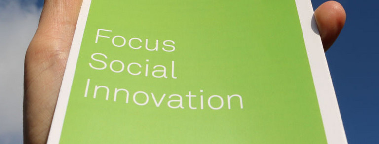 Der Schriftzug "Social Innovation" auf einem Flyer, der Richtung Himmel gehalten wird.