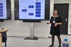 Foto: Eine Person steht in einem Seminarraum und präsentiert eine Folie auf einem großen Bildschirm. Die Folie enthält ein Diagramm mit Begriffen wie „Social Innovation“, „New Practices“ und „Transformation Path“.
