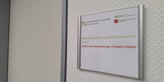 Stellenausschreibung w40/26 Deutsch Foto: Türschild mit Logos der TU Dortmund, der Fakultät Sozialwissenschaften und der sfs. Darunter der Text "Wisseschaftliche Mitarbeiter*in (m/w/d)" und "Arbeit in der Dienstleistungs-/Interaktionsarbeit". Neben dem Türschild ist eine geschlossene Tür.