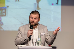 Podiumsdiskussion Eine Person steht an einem Rednerpult mit Mikrofon in der Hand