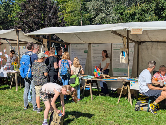 Das Bild zeigt einen Stand auf dem Quartiersfest, an dem sich Mieterinnen und Mieter zum Austausch treffen können. Davor hat sich eine kurze Schlange gebildet.