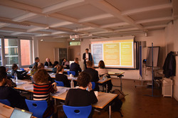 Foto: Vortrag in einem Seminarraum mit Teilnehmenden, die einer Präsentation folgen.