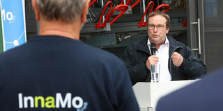 Oliver Krischer hält ein Mikrofon in der Hand und steht vor einem weißen Rednerpult