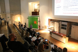 Foto: Personen sitzen in einem Hörsaal und folgen einer Präsentation auf einer Leinwand.