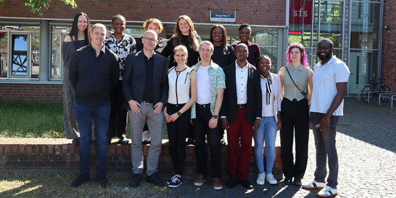 Group photo: 14 people standing in front of the sfs building