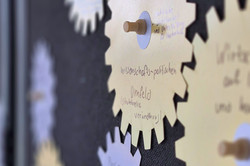 Foto: Auf einer Metaplantafel sind beschriebene Notizzettel in Form von Zahnrädern mit Pinnadeln befestigt.