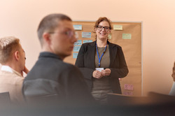 Zukunftsfabrik Bild 4 4 Personen sitzen vor einer Pinnwand. 1 andere Person steht mit dem Rücken zur Pinnwand vor ihnen.