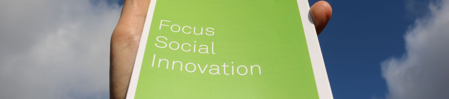 Der Schriftzug "Social Innovation" auf einem Flyer, der Richtung Himmel gehalten wird.
