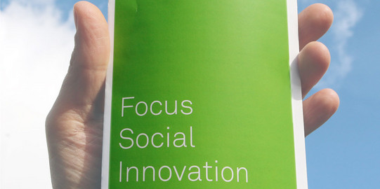A hand is holding a flyer with the text "Focus Social Innovation" on its cover.