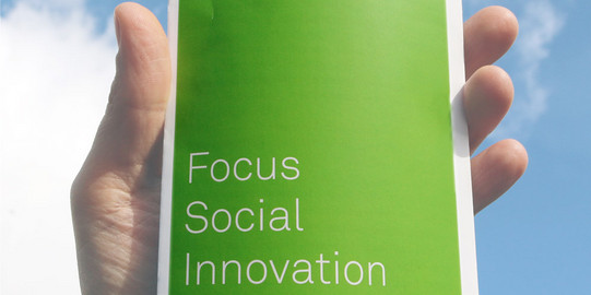Hand die einen Flyer hält auf dem "Focus Social Innovation" steht.