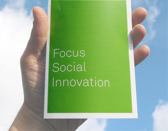 A hand is holding a flyer with the text "Focus Social Innovation" on its cover.