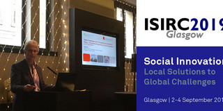 Vortrag von Prof. Jürgen Howaldt auf der ISIRC 2019 in Glasgow. Rechts neben ihm ist seine Powerpoint-Präsentation zu sehen.