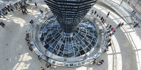 Bild der Kuppel des Bundestags aus größerer Höhe. In der Innenansicht der Kuppel sind zahlreiche Menschen innerhalb der Glaskuppel zu sehen.
