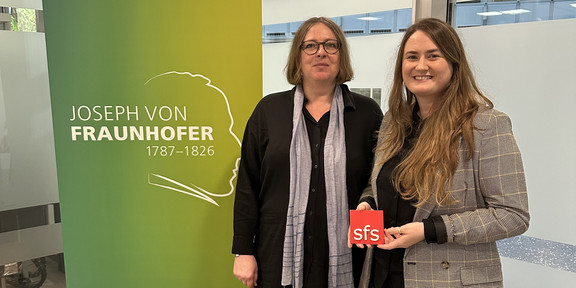 Photo: Lisa-Marian Schmidt and Christine Best standing next to a roll-up banner from the Fraunhofer Institute