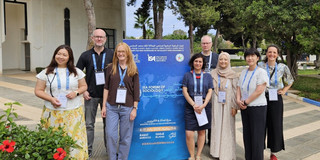 Group photo ISA The eight participants in the panel discussion stand next to a display stand for the ISA conference.