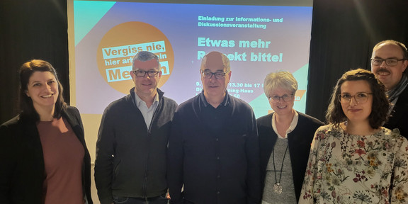 Foto: Gruppe von Personen steht vor einer Leinwand mit Informationen zu einer Diskussionsveranstaltung.