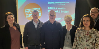 Foto: Gruppe von Personen steht vor einer Leinwand mit Informationen zu einer Diskussionsveranstaltung.