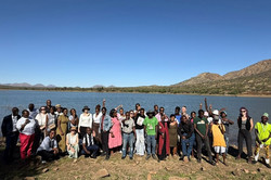 Gruppenfoto einer großen Gruppe auf einem Felsen vor einem See und Bergen