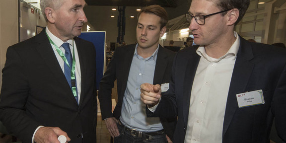 Foto: Drei Personen unterhalten sich bei einer Veranstaltung in einem großen Saal.