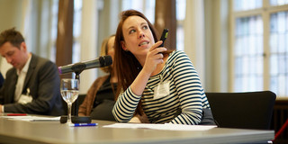 Foto: Marthe Zirngiebl spricht bei einer Veranstaltung in einem Konferenzraum und hält ein Präsentationsgerät.