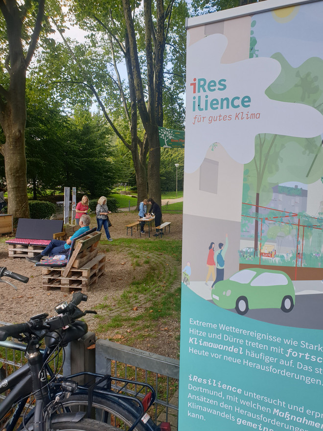 Klimaoase im Blücherpark in der Dortmunder Nordstadt mit Sitzgelegenheiten unter Bäumen und einem Schild vom Projekt "iResilience"