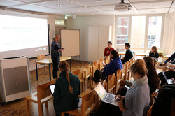 Foto: Vortrag in einem Seminarraum mit Teilnehmenden, die zuhören und Notizen machen.