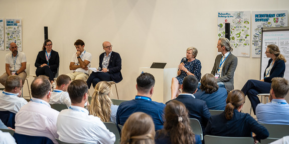 Podiumsdiskussion mit 7 Teilnehmenden und Publikum