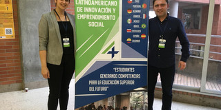 Sabrina Janz und Dmitri Domanski von der Sozialforschungsstelle Dortmund stehen im Rahmen des Projektes „Students4Change“ bei ihrem Aufenthalt in Bogotá lächelnd neben einem Aufsteller.