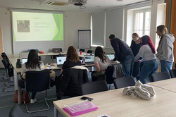 7 Personen sitzen an Laptops in einem Konferenzraum
