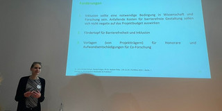 Ann-Christin Schulz is giving a lecture. Next to her, a presentation is being projected onto the wall using a projector.
