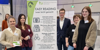 Marie-Christin Lueg, Dr. Vanessa Heitplatz, PD Dr. Bastian Pelka, Miriam Wüst und Nele Maskut stehen im Halbkreis um einen 2m hohen Banner. Auf ihm wird auf Easy Reading und das Projekt EVE4all aufmerksam gemacht. Im Hintergrund sind weitere Banner und Messebesucher.