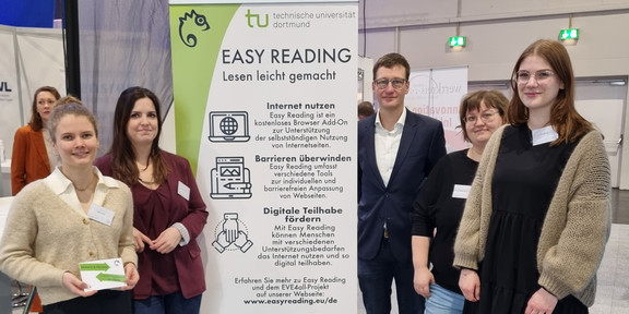 Marie-Christin Lueg, Dr. Vanessa Heitplatz, PD Dr. Bastian Pelka, Miriam Wüst und Nele Maskut stehen im Halbkreis um einen 2m hohen Banner. Auf ihm wird auf Easy Reading und das Projekt EVE4all aufmerksam gemacht. Im Hintergrund sind weitere Banner und Messebesucher.