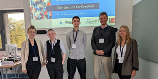 Foto: 5 Personen stehen vor einer Präsentation auf einer Leinwand