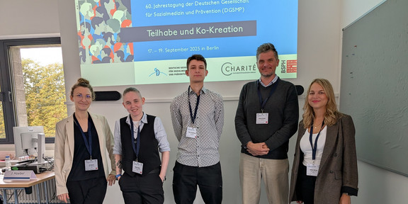 Foto: 5 Personen stehen vor einer Präsentation auf einer Leinwand