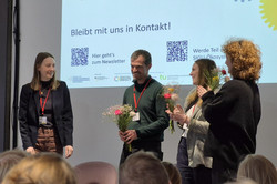 Photo: Four people are standing in front of an audience; three of them are holding bouquets of flowers.