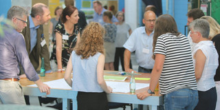 A group of people have a conversation standing at a table at a project event.