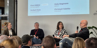 A large audience of participants from the Zukunftsfabrik listens to the panel, consisting of PD Dr. Christoph Kaletka from the SFS, Viola Stegmann (SEND e.V.), and Norbert Kunz (Social Impact gGmbH). The discussion is moderated by Kiara Sobina (Social Impact gGmbH).