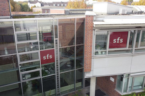 Drohnenaufnahme der verglasten Rückseite der Sozialforschungsstelle Dortmund an der Deutschen Straße in Eving mit zwei roten sfs-Logos