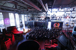 Foto: Veranstaltung mit Publikum in einer großen Industriehalle mit Bühne und Beleuchtung.