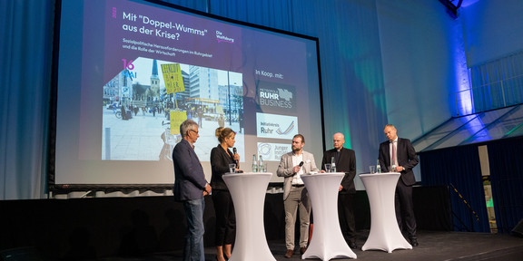 Podiumsdiskussion 4 Personen stehen auf einer Bühne