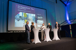 Podiumsdiskussion 4 Personen stehen auf einer Bühne