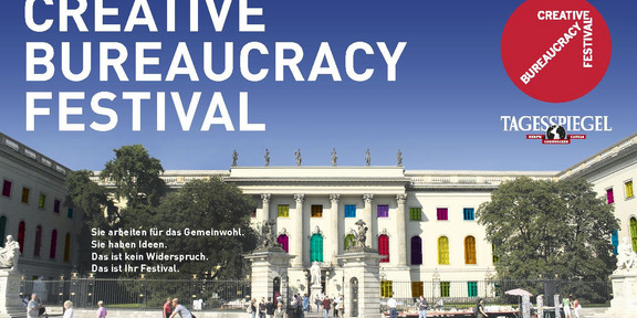 Hauptgebäude der Humboldt-Universität zu Berlin mit bunten Fenstern bei sonnigem Wetter. Schriftzug "Creative Buraucracy Festival". Darunter steht: "Sie arbeiten für das Gemeinwohl. Sie haben Ideen. Das ist kein Widerspruch. Das ist Ihr Festival."