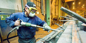 Man with respirator, goggles and glove on left hand works in a workshop.