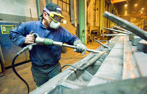 Man with respirator, goggles and glove on left hand works in a workshop.