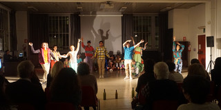 Verkleidete Menschen im Scheinwerferlicht tanzen vor einem Publikum