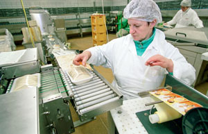 Employee with white protective clothing and white hair cap works on the assembly line and labels products.