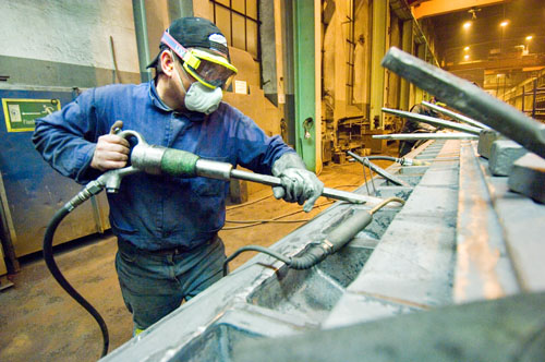 Man with respirator, goggles and glove on left hand works in a workshop.