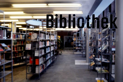 Blick in die Bibliothek der Sozialforschungsstelle. In schwarzen Schrift rechts oben das Wort „Bibliothek“